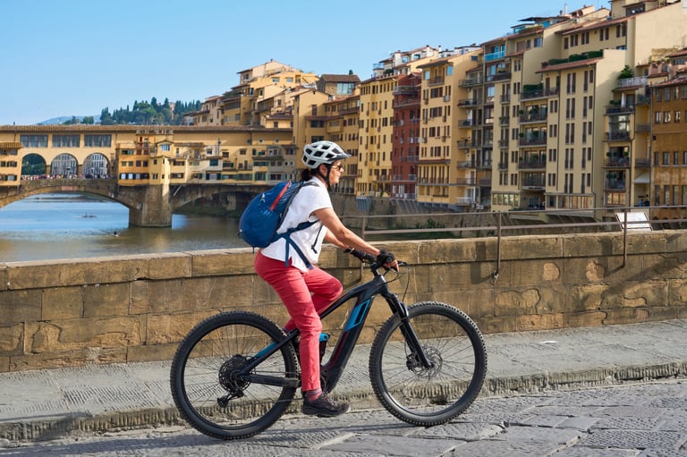 Mulher sorridente pedalando com bicicleta elétrica no centro histórico de Florença com a famous ponte Vecchio ao fundo, Toscana, Itália