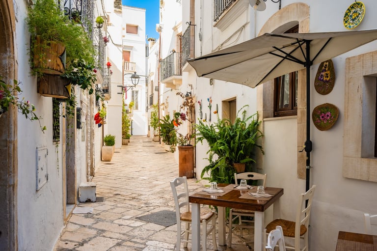 Locorotondo Italy - Cozy cafe tables in whitewashed alley with plants and flowers