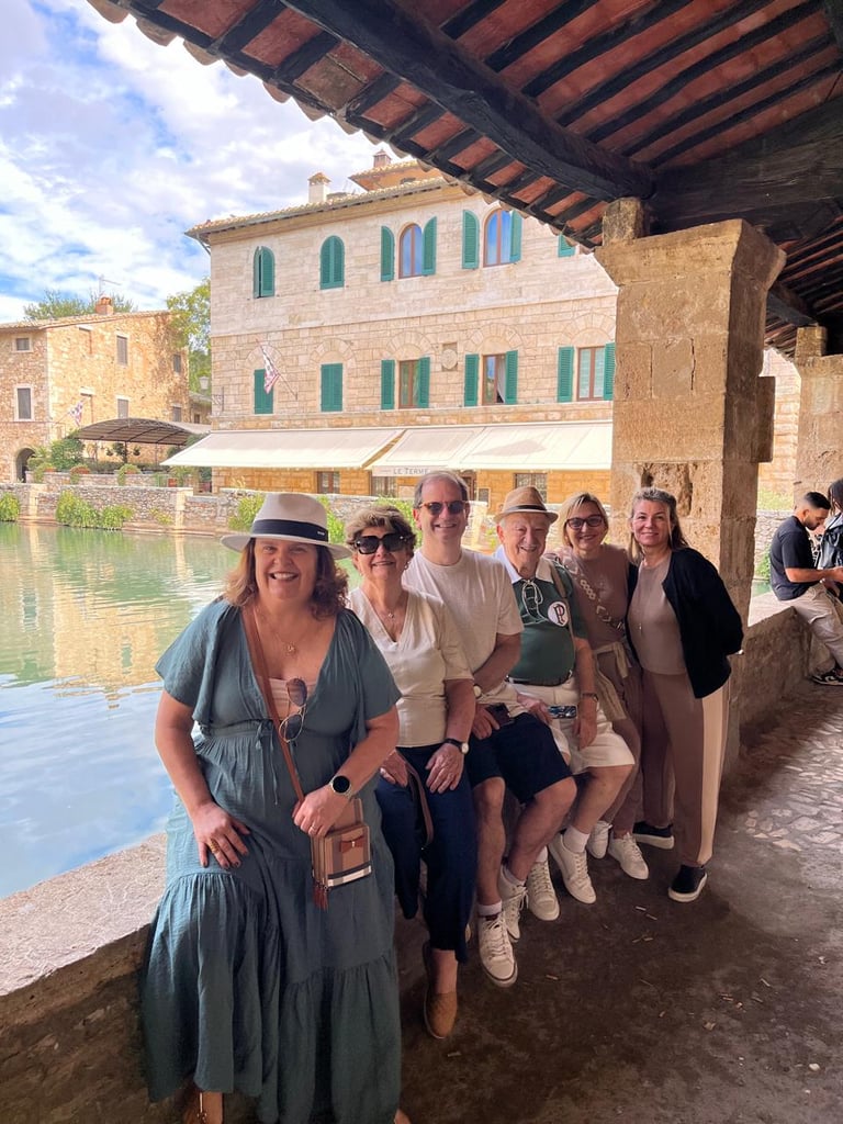 Group of tourists posing by a canal with historic Italian stone buildings and green shutters in the background
