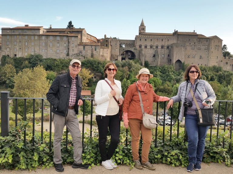 Three tourists standing at a railing with a medieval hilltop castle and historic town buildings in the background