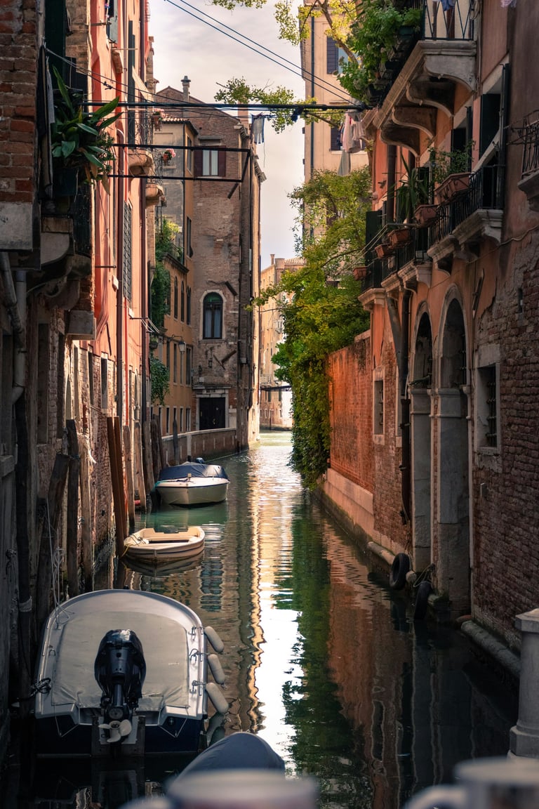Blue and orange boat in a narrow Venice canal flanked by aged brick buildings and a stone bridge