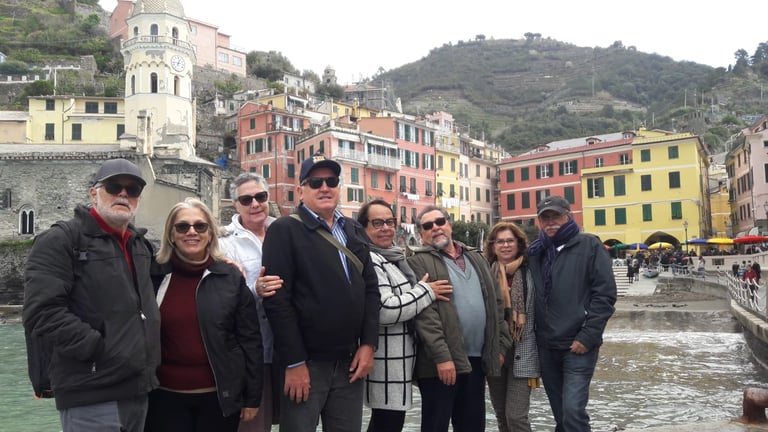 Group of tourists posing together in Vernazza, Cinque Terre, with colorful waterfront buildings and mountains in the background